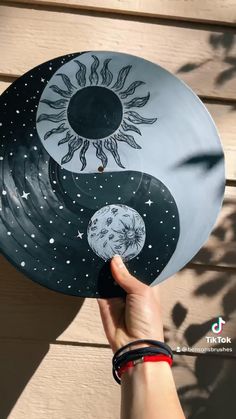 a person holding up a plate with the sun and moon painted on it's side