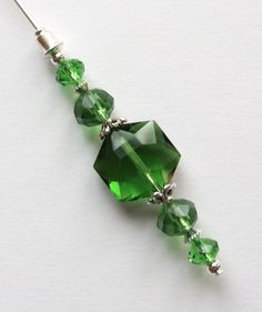 a green beaded necklace on a white surface with silver beads and crystal stones hanging from it's end