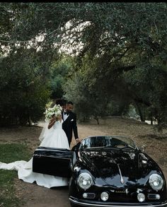 a bride and groom standing next to a black car