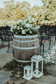 a wooden barrel with flowers on it next to two small white lanterns and some chairs