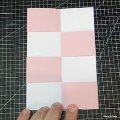 someone is cutting out pink and white squares on a piece of paper that has been cut into smaller squares