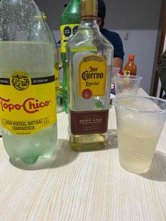 two bottles of alcohol sitting on top of a table next to a glass filled with water