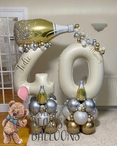 a teddy bear is standing next to balloons and champagne bottles in the shape of numbers