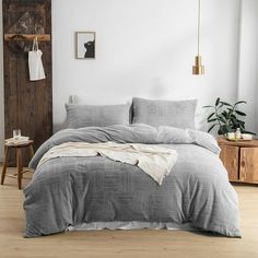 a bedroom with white walls and wooden floors has a gray comforter on the bed