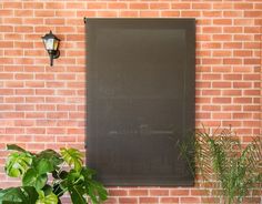 a brick wall with a black window and potted plants on the ground next to it