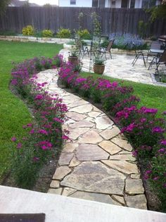 a stone path in the middle of a garden with purple flowers growing on each side