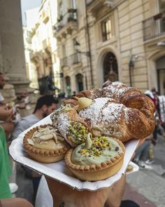 a person holding up a tray with pastries on it in front of people walking down the street