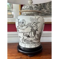 a white and black vase sitting on top of a wooden table next to a lamp