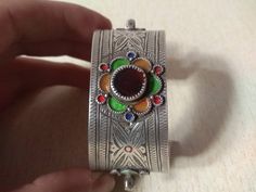 This is a Beautiful silver berber bracelet from the Anti Atlas region in Morocco. The decoration is very refined, there's some remains of black deco and enamel in yellow and green. This bracelet shows an exquisite quality of engraved work with flower motifs. The center stone is an glass in red color. Min Width : 2,5 cm (0,98 inches) Max Width : 4,2 cm (1,6 inches) Inner diameter : 5,8 cm (2,3 inches) Weight : 56,7 g Silver Meenakari Bangle Bracelet, Bohemian Silver Bracelets With Meenakari, Ornate Multicolor Bracelets For Gifts, Ornate Multicolor Bracelet For Gift, Traditional Black Enamel Jewelry For Gift, Traditional Black Enamel Jewelry Gift, Traditional Multicolor Enamel Bracelets, Traditional Silver Enamel Bangle, Traditional Inlay Cuff Bangle Bracelet