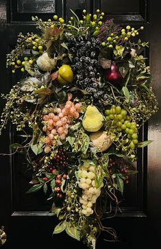 a bunch of fruit is hanging on the front door with leaves and berries around it