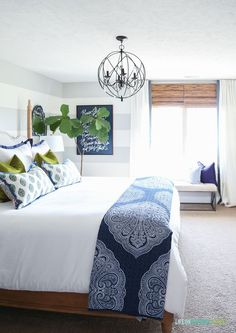 a bedroom with white bedding, blue and green pillows and a chandelier hanging from the ceiling