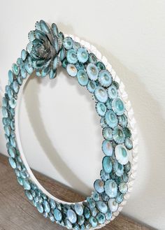 a blue and white wreath made out of glass beads on a wooden table next to a wall