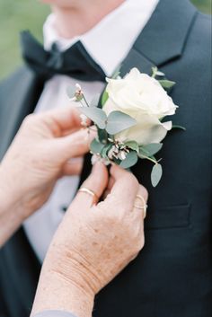 an older woman is adjusting the boutonniere on her groom's lapel