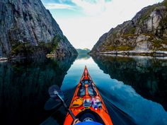 an orange kayak is in the middle of a lake surrounded by mountains and cliffs