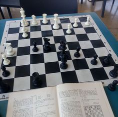 a chess board with pieces on it and an open book in front of it, sitting on a table