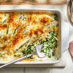 a casserole dish with green vegetables and cheese in it on a white table