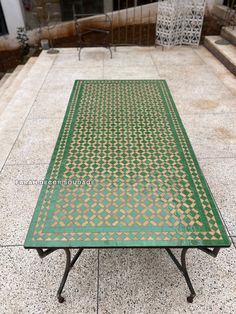 a green table sitting on top of a tiled floor next to stairs and steps in front of a building