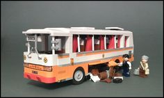 a toy bus with two people standing next to it and one person sitting on the ground