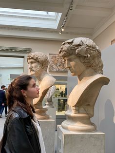 a woman standing next to two busts in a room with other statues on the walls