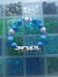 a plastic container filled with lots of different colored beads next to a white and blue beaded bracelet