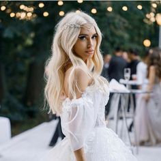 a woman with long blonde hair wearing a white dress in front of a table full of people