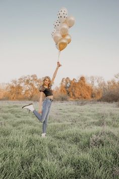 a woman is jumping in the air with some balloons on her head while holding onto two white and gold balloons