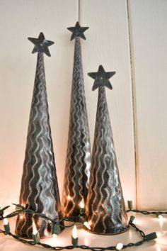 three metal cone shaped christmas trees with lights on the ground in front of white wall