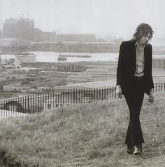 a woman walking on top of a grass covered hillside next to a fenced in field