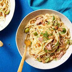 a bowl of pasta with meat and vegetables on a blue tablecloth next to a wooden spoon