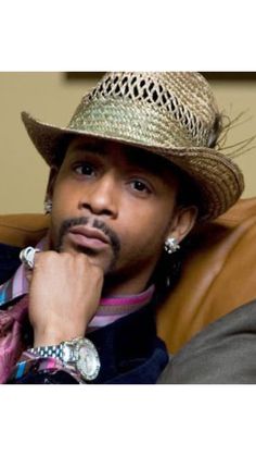 a man wearing a hat sitting on top of a brown leather couch with his hand under his chin