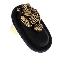 a gold turtle brooch sitting on top of a black velvet case with an ornate design