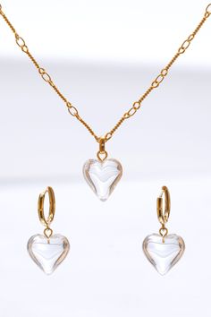 This stunning set features a beautifully crafted heart-shaped pendant adorned with shimmering crystal, hanging gracefully from a delicate gold chain. The matching earrings mirror the pendants' design, offering a perfect balance of sophistication and charm. Ideal for both everyday wear and special occasions, this set effortlessly enhances any outfit with a touch of timeless glamour. Handmade item 18k gold plated brass Syn crystal Hypoallergenic 925 silver post Necklace length: 42cm+6cm extension Elegant Clear Jewelry For Valentine's Day, Gold Double Heart Crystal Jewelry, Gold Plated Heart Pendant Earrings, Elegant Gold Crystal Heart Earrings, Gold Crystal Heart Necklace, Gold Crystal Heart Pendant Necklace, Gold Crystal Heart Pendant Jewelry, Gold Plated Heart Charm Necklace For Valentine's Day, Clear Heart Pendant Jewelry For Valentine's Day