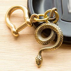 a gold snake keychain sitting on top of a wooden table next to a cell phone