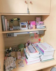 a wooden desk topped with lots of books next to a shelf filled with other items