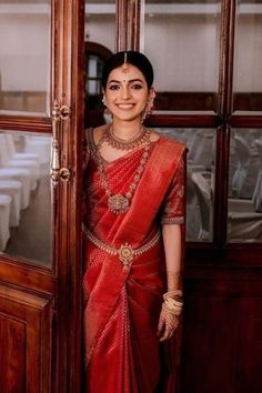 a woman standing in front of a wooden door wearing a red sari and gold jewelry