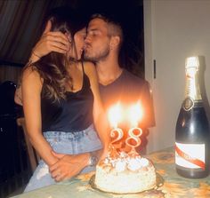 a man and woman kissing in front of a birthday cake with candles on it, next to a bottle of booze