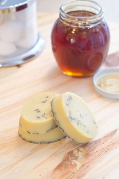 two pieces of cheese sitting on top of a cutting board next to a jar of honey