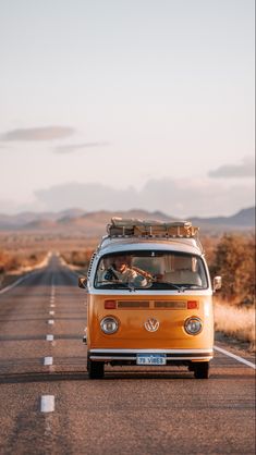 an orange vw bus driving down the road with luggage strapped to it's roof