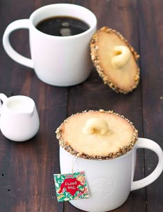 two mugs filled with coffee and cookies on top of a wooden table next to each other