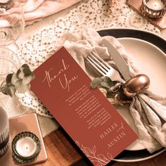 a place setting with an orange menu card and silverware on the plate, next to a candle