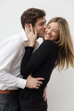 a man and woman kissing each other while standing next to each other in front of a white wall