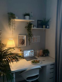 a white desk topped with a laptop computer next to a potted plant and lamp