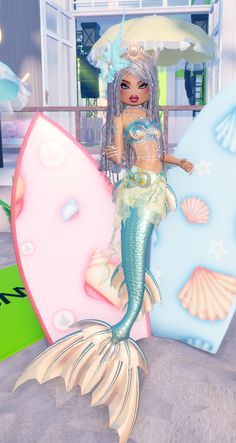 a mermaid doll sitting on top of a surfboard next to a giant letter shaped like a fish