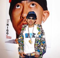 a young man with sunglasses and a hat on standing in front of a large poster