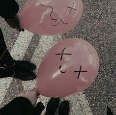 two balloons with faces drawn on them are being held by someone's feet in the street