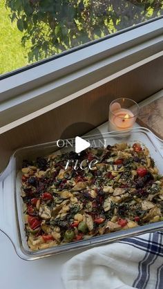 a casserole dish is sitting on a window sill next to a candle