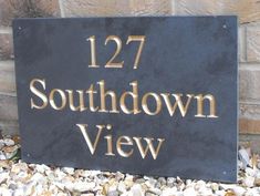 a black and gold sign sitting on the side of a brick wall next to gravel