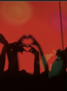 the shadow of two hands making a heart shape in front of a red background with an orange sky