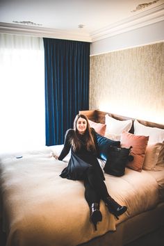 a woman sitting on top of a bed in a bedroom next to a blue curtain