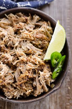 a bowl filled with shredded meat next to a slice of green pepper and a lime